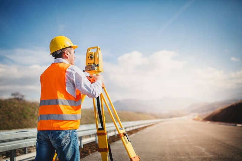 Professional land surveyor using a total station on a construction site during field surveying work in Madison, AL.